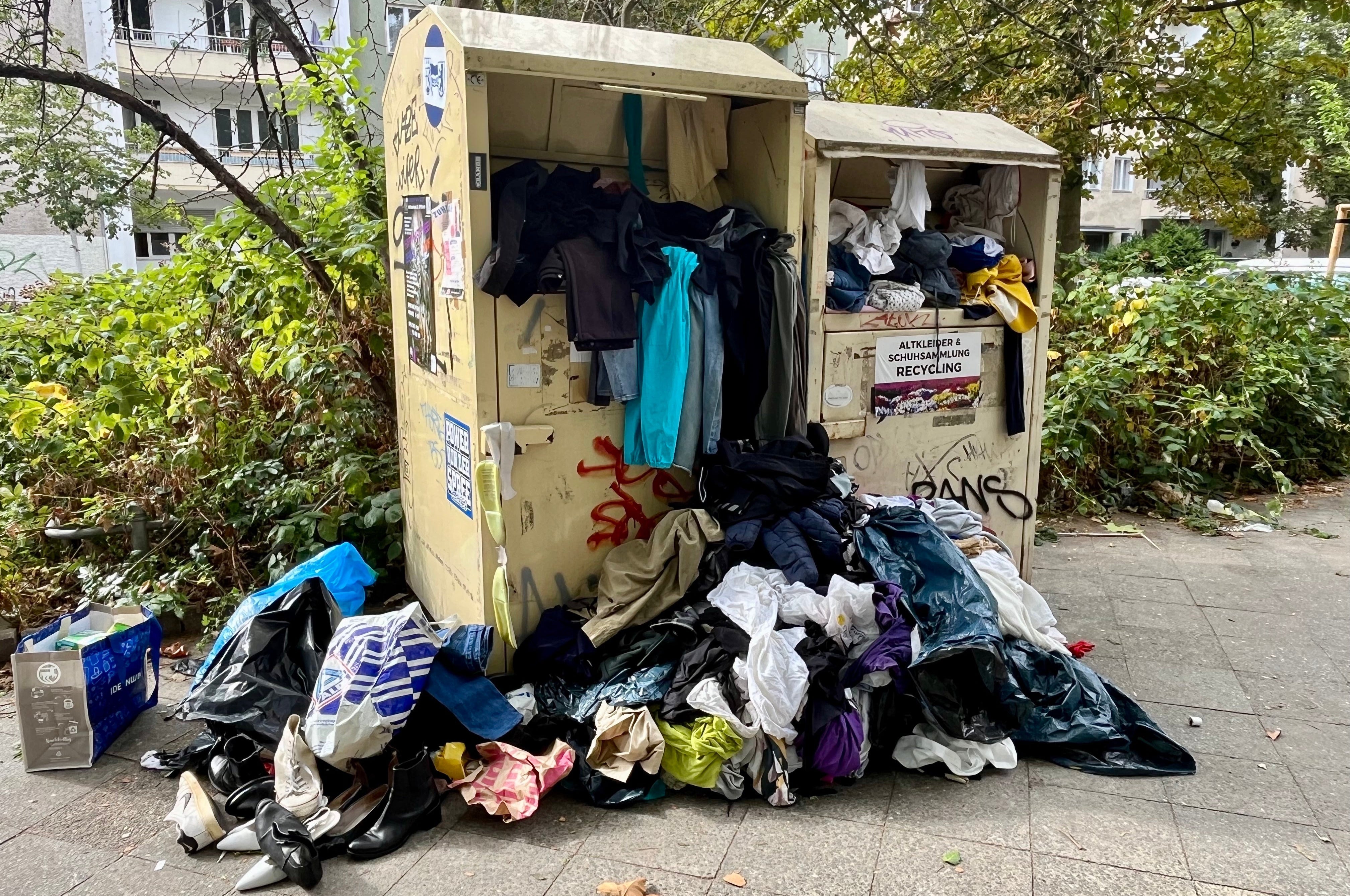 Altkleider vor einem überfüllten Altkleidercontainer
